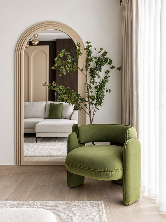 Green lounge chair and plants beside an arched mirror